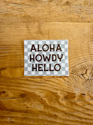 Sticker with 'Aloha Howdy Hello' text and a checkered background. 