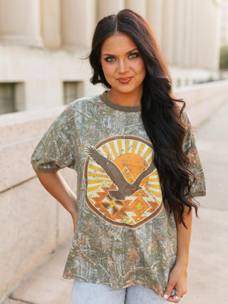 Woman wearing a camouflage t-shirt with a graphic design of an eagle and sun.