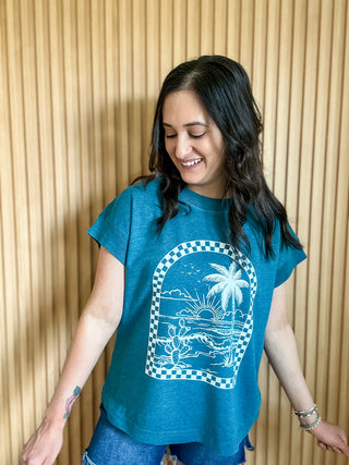 Oceanside colored women's relaxed tee with a white checkered arch design with a coastal scene inside the arch. 