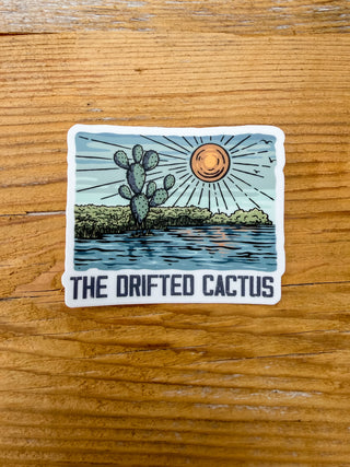 Sticker with a cactus on the shoreline and the sun in the background and The Drifted Cactus text below. 