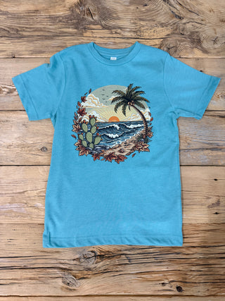 A turquoise blue youth size short-sleeve t-shirt with a circular graphic print of a beach scene featuring a palm tree, cacti, and waves, and fall leaves to make it a coastal fall tee.