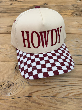 A beige baseball cap with 'HOWDY' embroidered in maroon on the front, featuring a maroon and white checkered brim. 